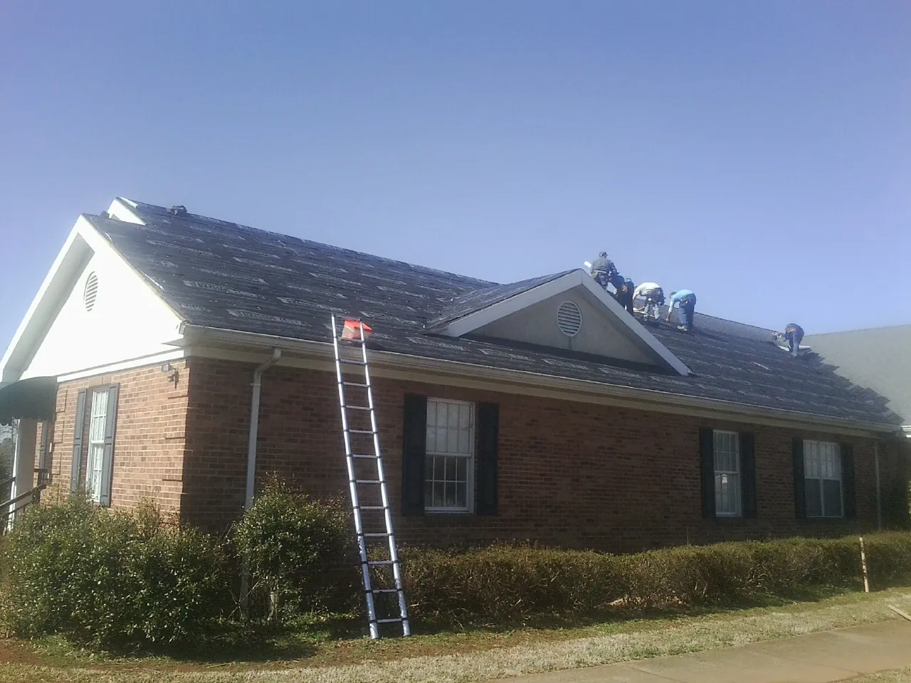Crew tearing shingles off a brick ranch roof with a ladder set — Emergency Roof Repair work by our crew in Marlboro