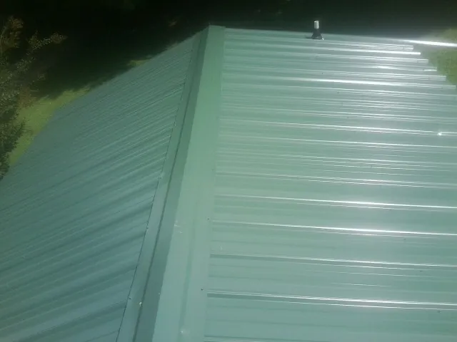 New green metal panels meeting at the ridge of a roof — Flat Roof Repair work by our crew in Marlboro