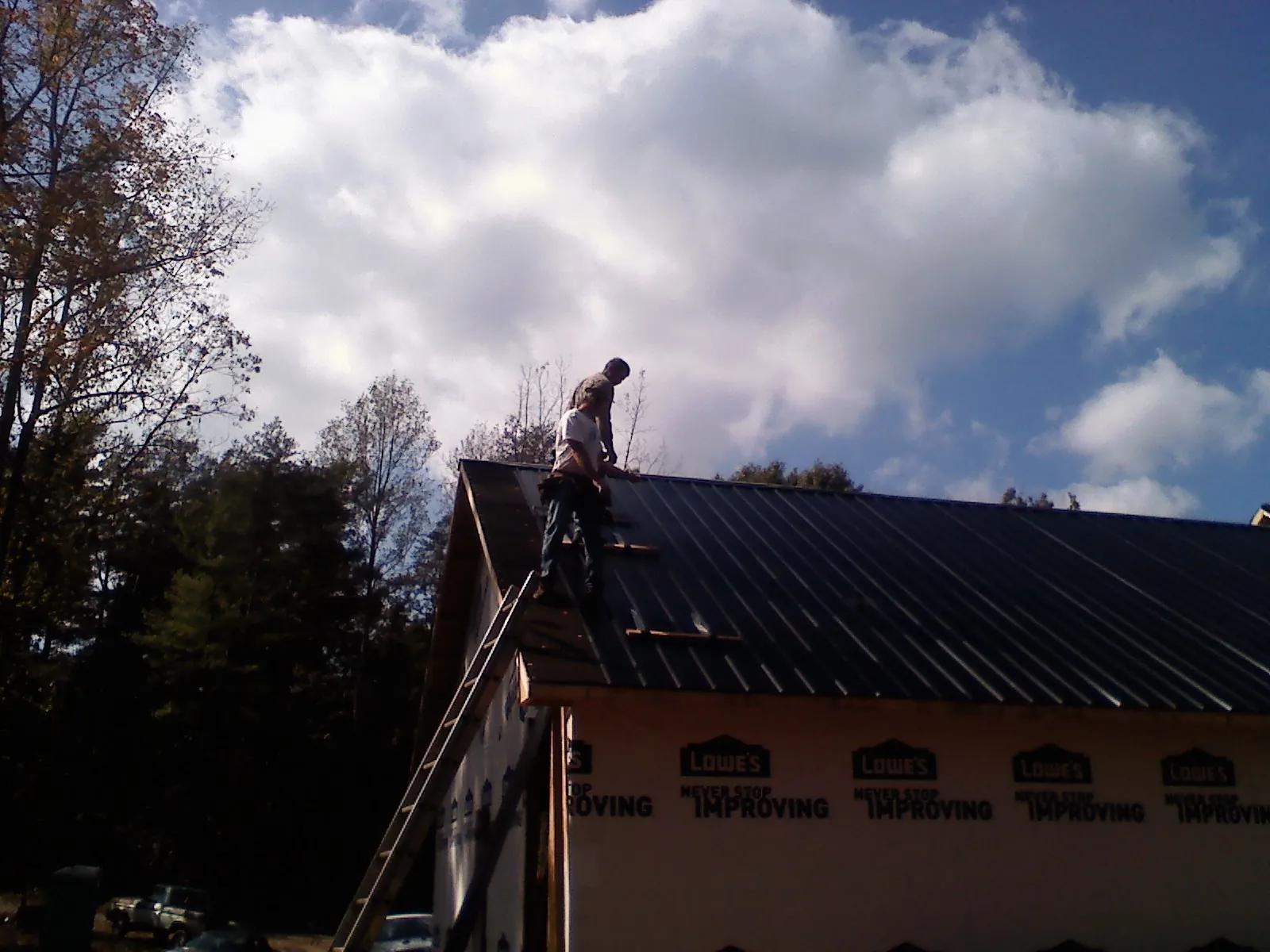 Roofer fastening dark metal panels high against a cloudy sky, from a Roof Inspection job in Marlboro