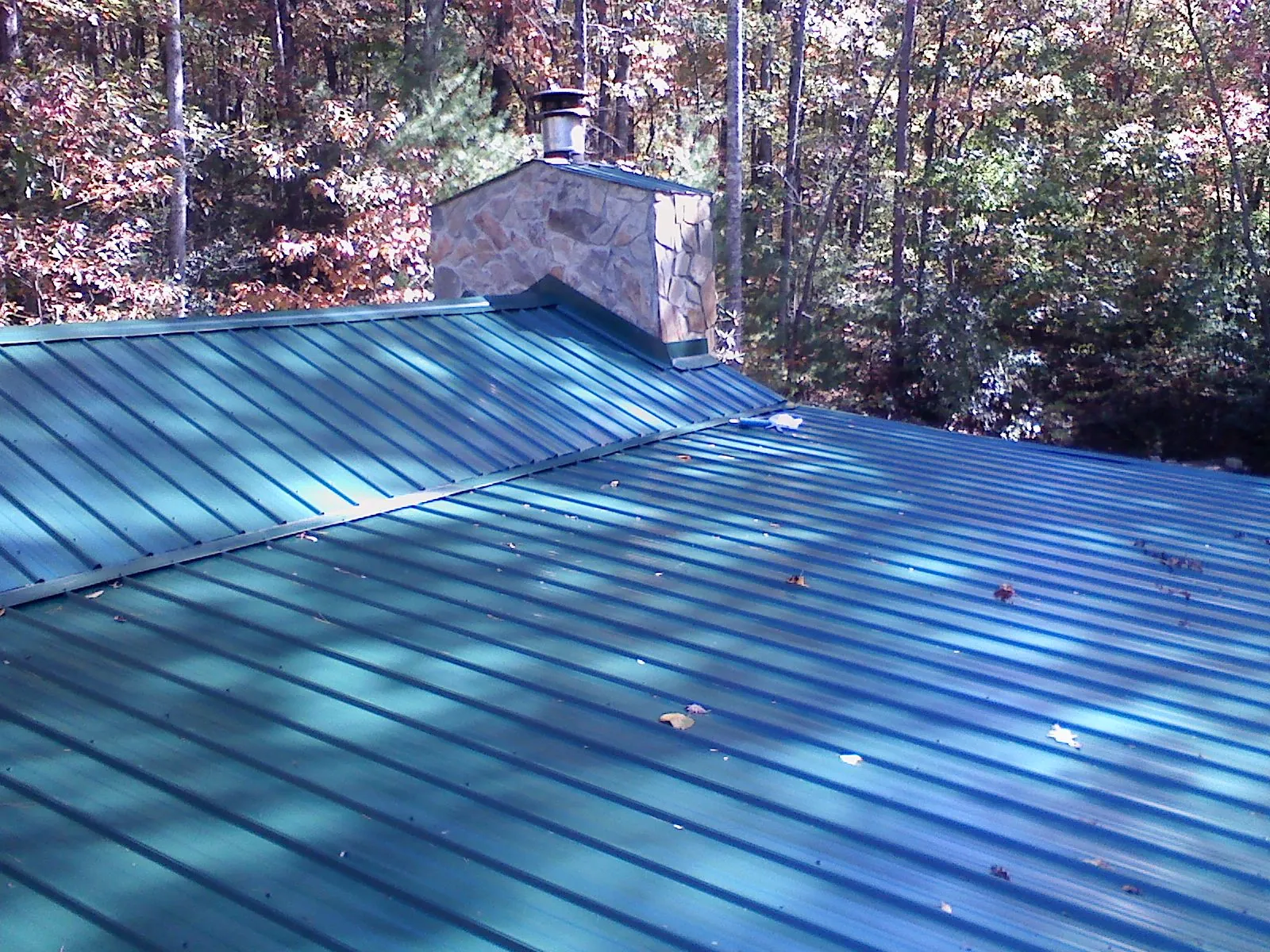 New green metal roof and stone chimney surrounded by autumn woods in Marlboro