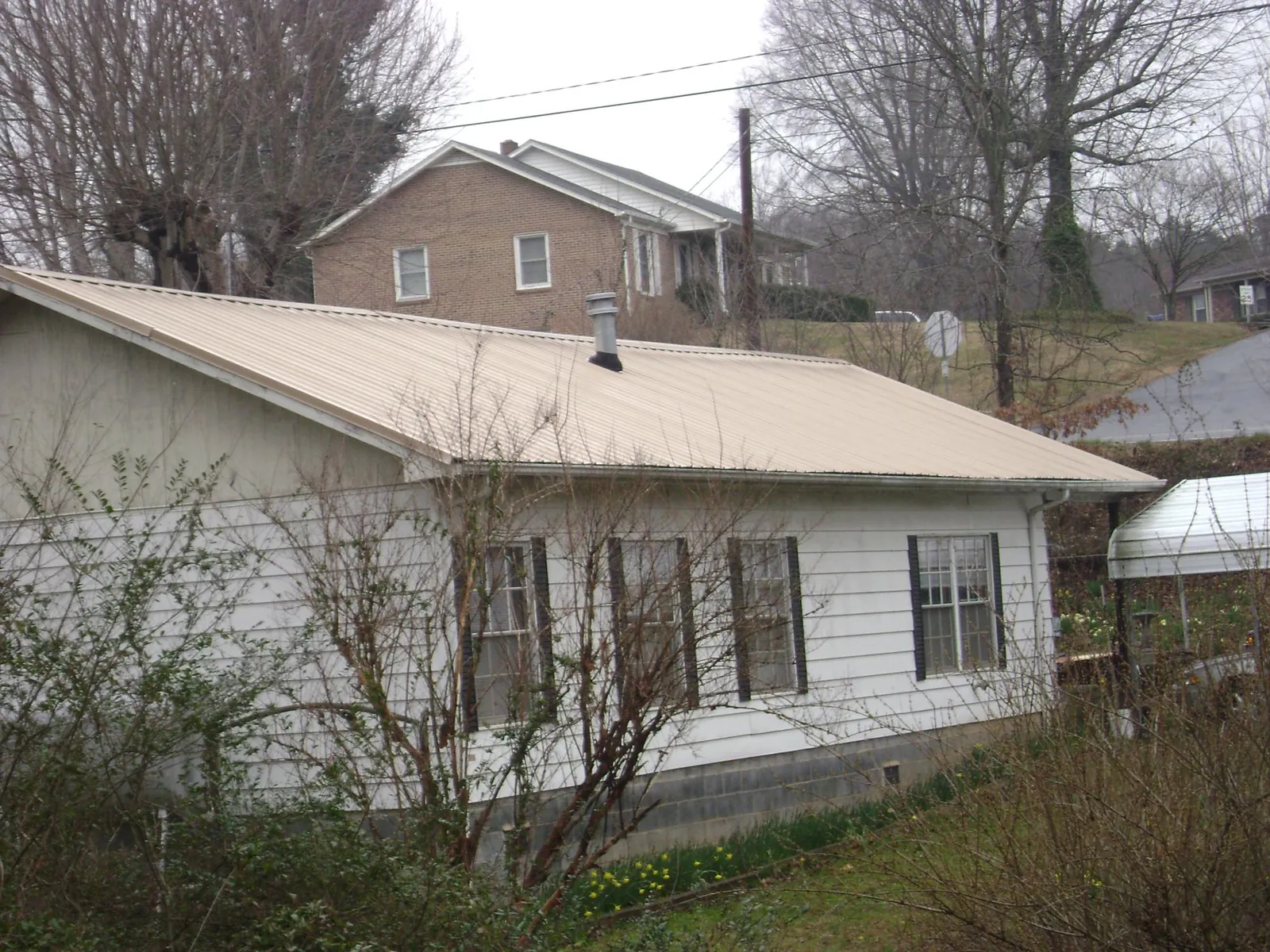 Tan metal roof on a white sided house set into a hillside — Commercial Roofing by Roofing Brothers in Marlboro